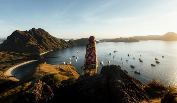 A lone traveler enjoys a stunning sunrise on Padar Island, Indonesia, overlooking the tranquil bay and surrounding landscape.
